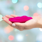 A hand holding the compact and vibrant pink OhMiBod Foxy Bluetooth Panty Vibrator against a blurred background with soft, colorful lights hints at OhMiBod's innovative Velvet Wave technology.